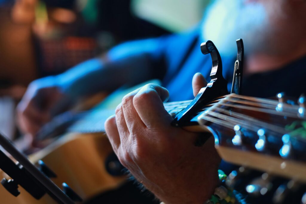 Detailed view of hands playing guitar with capo, capturing musician's skill and emotion.